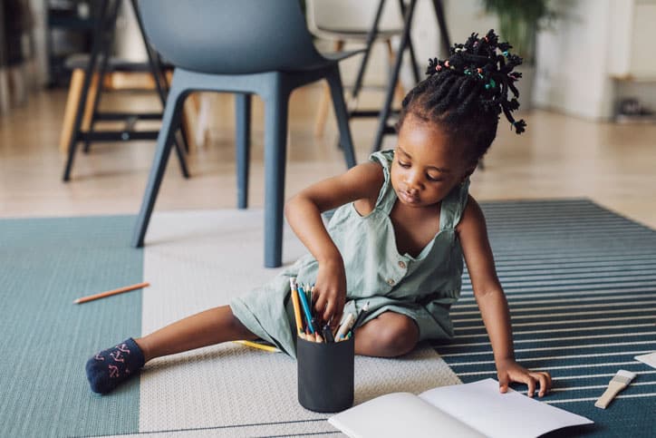 Close up shot of an young African American girl using coloured pencils drawing on the floor