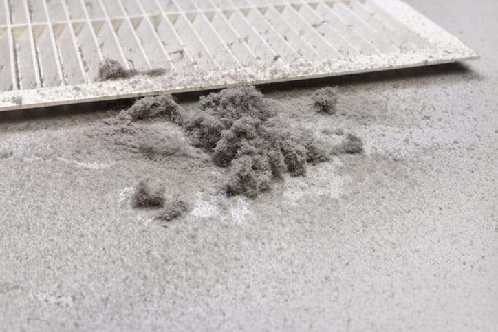 A close-up of a dirty air filter lying on a surface, with a pile of gray dust and debris around it—a reminder to prioritize carpet cleaning, especially before baby arrival.