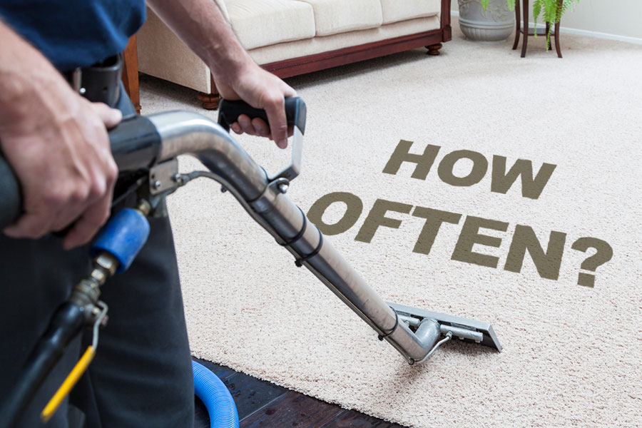 A person uses a carpet cleaning machine on a beige carpet with the words HOW OFTEN? written on the carpet, illustrating a homeowner’s guide to how frequently you should clean your carpets.